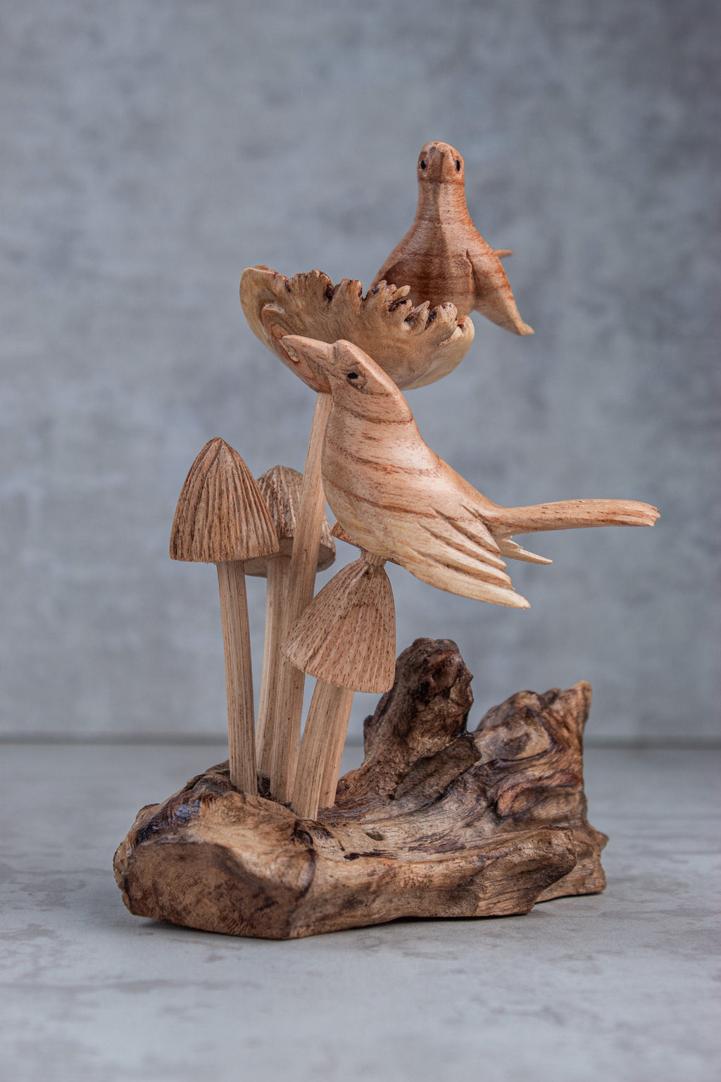 Wooden sculpture of a bird and plants on a textured surface with a gray background