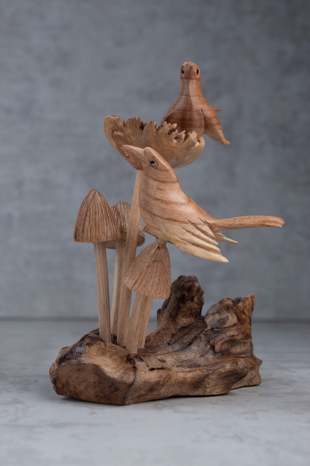 Wooden sculpture of birds and mushrooms on a natural wood base against a gray background