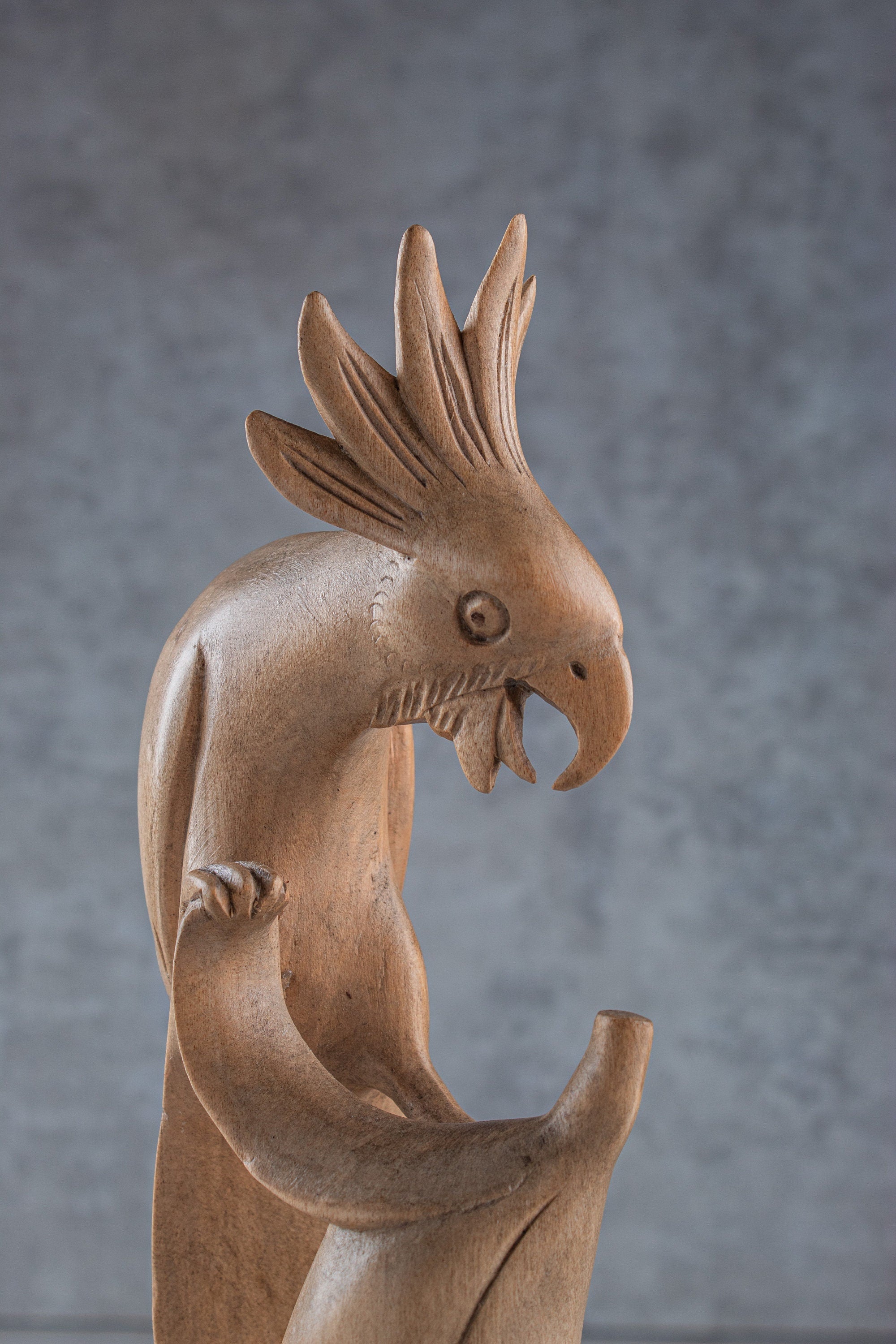 Brown wooden sculpture of a cockatoo with long neck and spiky head against a gray background