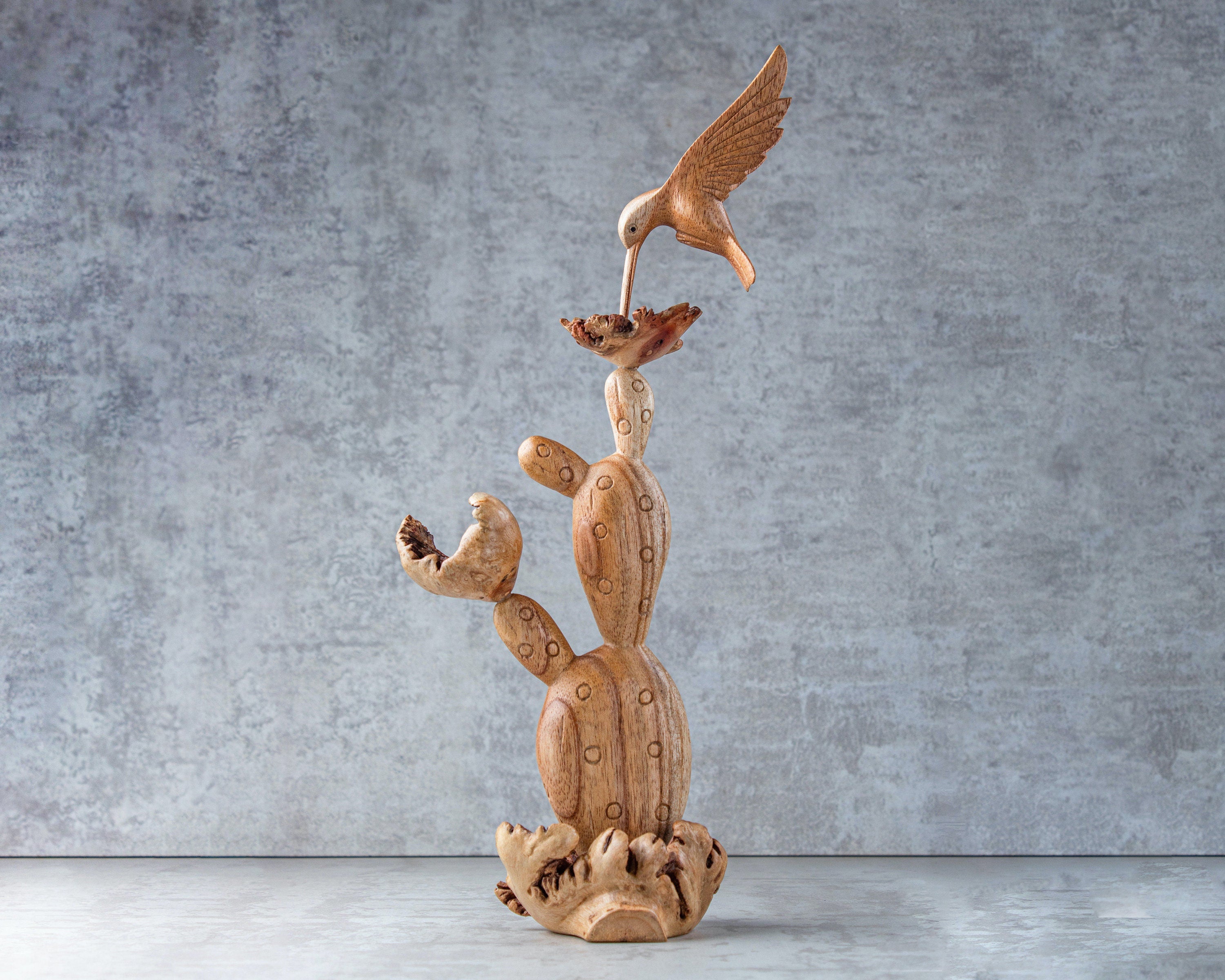 Wooden sculpture of a cactus with a bird on top against a gray background