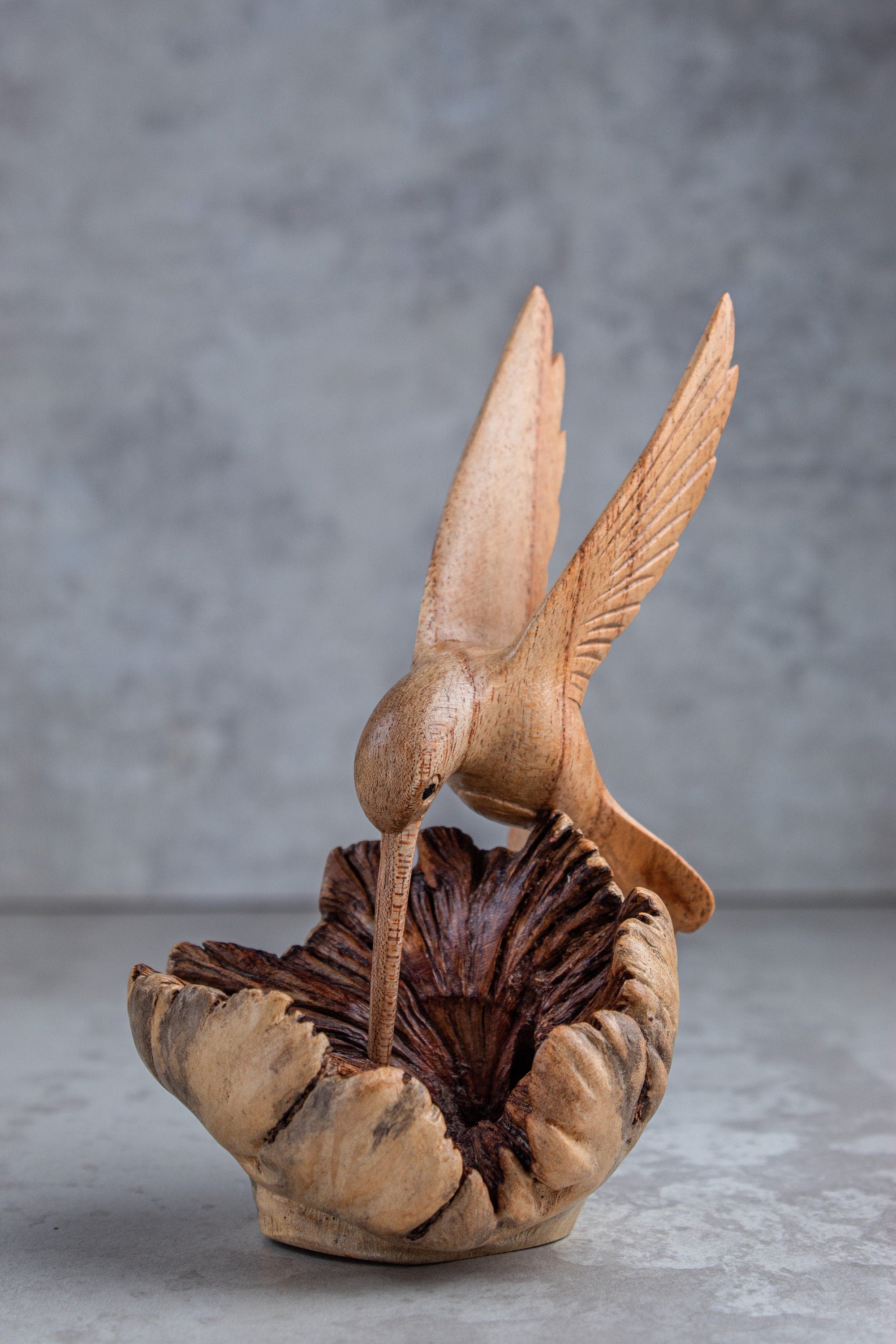 Wooden sculpture of a hummingbird on a nest against a gray background
