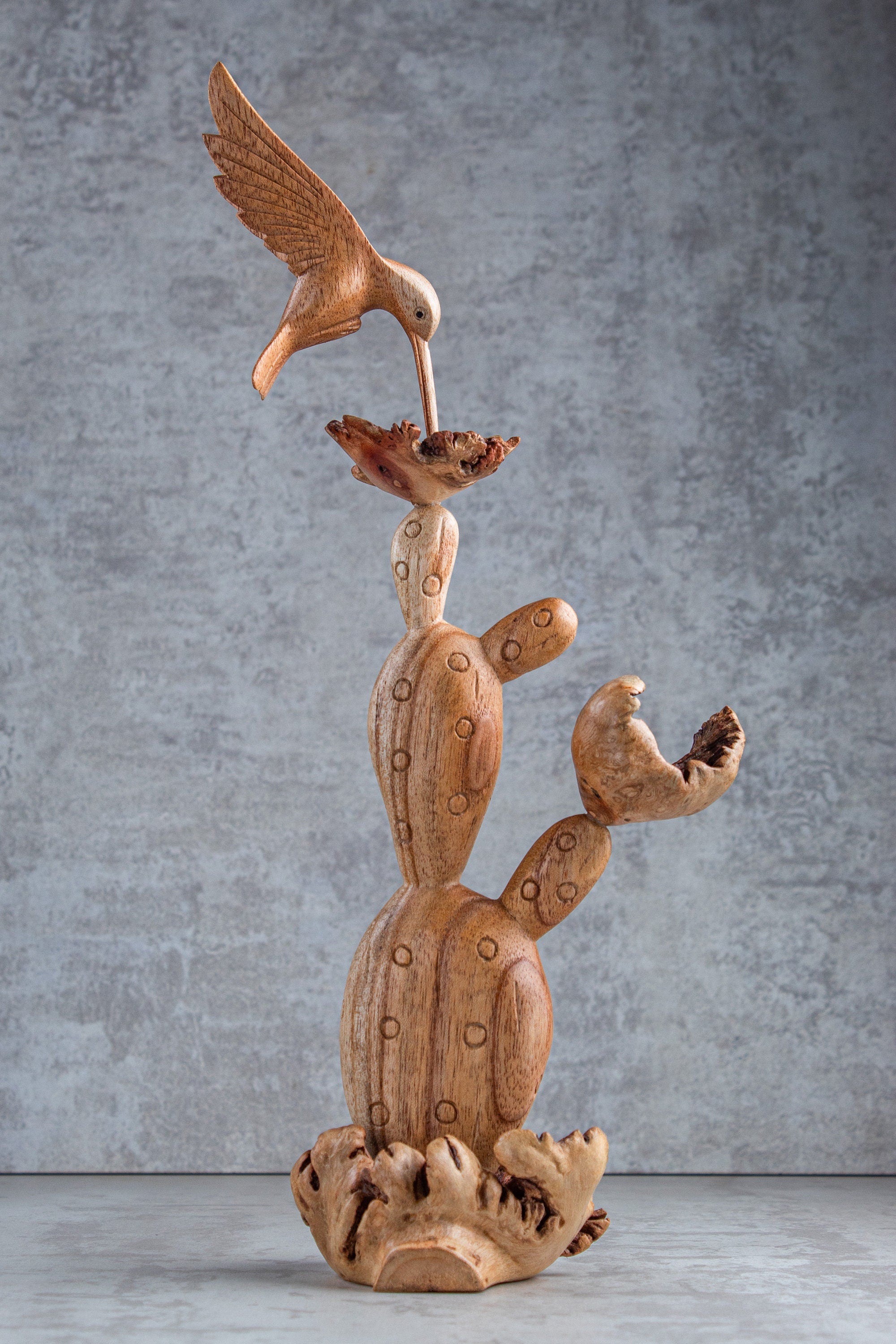 Wooden sculpture of a hummingbird and cactus on a gray background